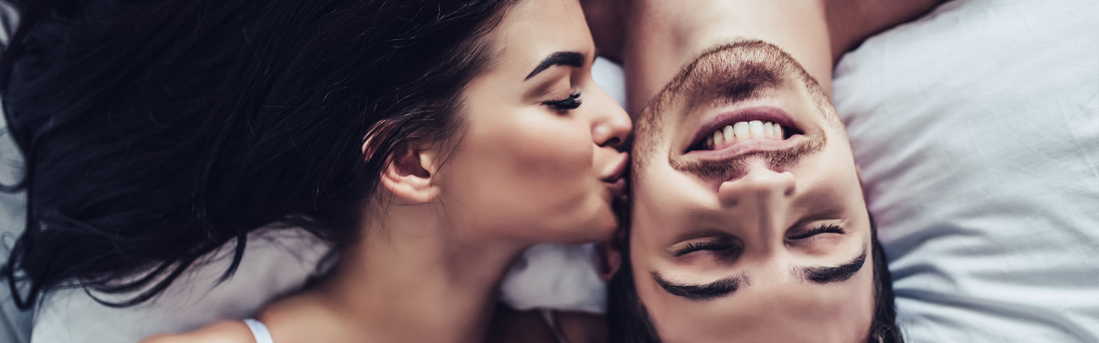 Woman kissing man's cheek in bed