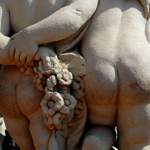 Butt shot of two stone cherubs holding hands behind themselves