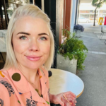 Clementine Ford sits at a cafe table with a drink in hand