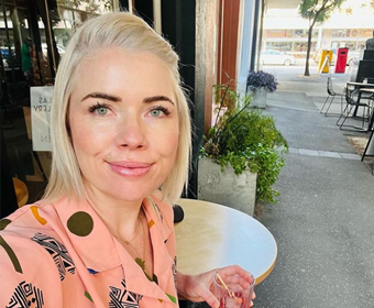 Clementine Ford sits at a cafe table with a drink in hand
