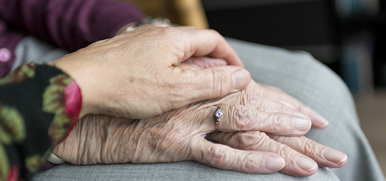 Image of older hands, wrinkled with age. One person's hand is sitting atop another person's in a gesture of care.