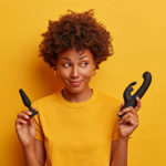 A woman smiles as she holds up two vibrators