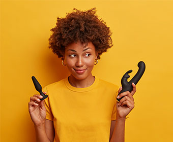 A woman smiles as she holds up two vibrators