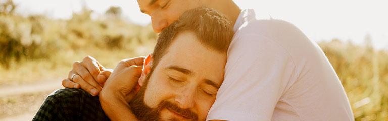 Two men embrace in a sunlit park. Making time to relax and unwind together - or separately - will help foster intimacy by giving you energy to spend with each other - and on other social commitments