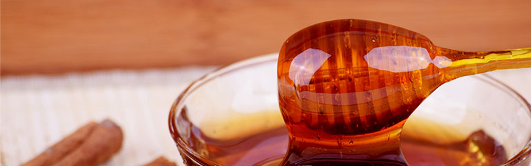 A honey dipper coated in honey sits on top of a glass of liquid honey. Honey makes a great edible date idea.