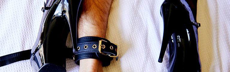 A man is cuffed to the bed by the Forte wrist & ankle cuffs from the Orchestra Pleasure Collection.