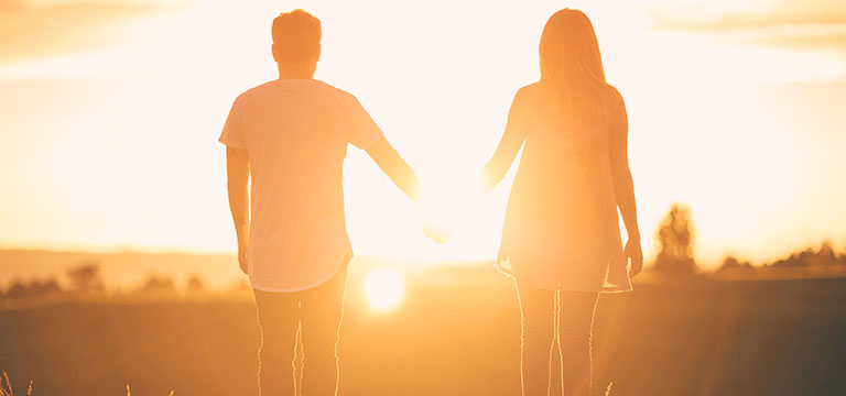 Two people hold hands as they look into the sunset. For many understanding that attraction and arousal are actually two separate experiences can really help with understanding asexuality