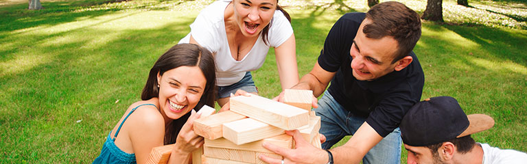 A group of friends play giant jenga in a sunlit park