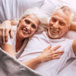 An older couple lie together in bed