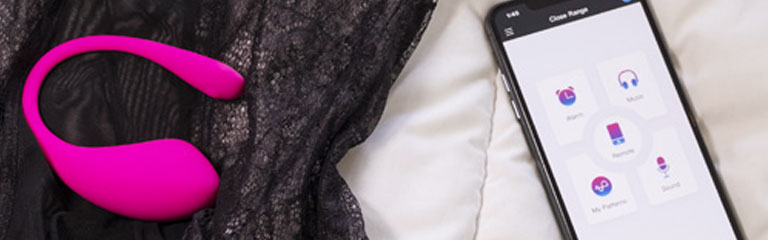 A Lovense Lush 3 bullet vibe lies on top of lingerie, next to a phone with the app for controlling it loaded on screen.
