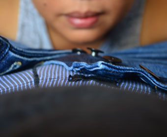 A person's lips hover over the unbottuned fly of their partner's jeans, showing striped underwear beneath