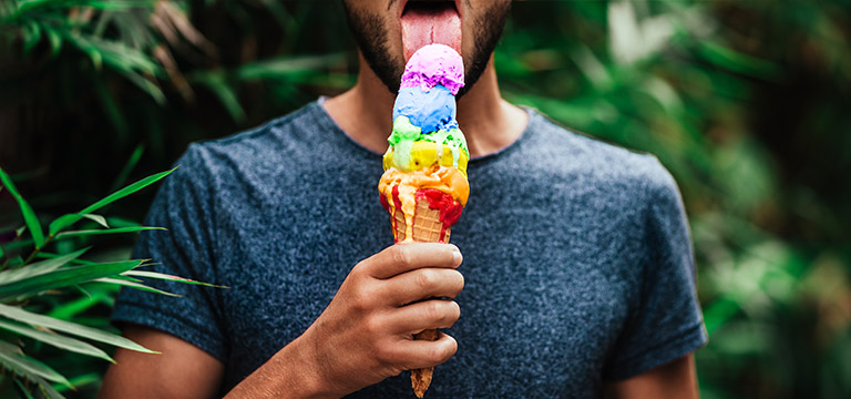 A bearded man licks a cone piled high with rainbow coloured ice cream. Food sex can be as simple as eating something suggestively.