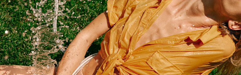 A woman lies back on the grass with a hose showering her with water, simulating squirting.