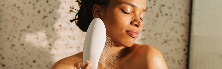 A woman holds the Womanizer Wave shower head up to her torso.