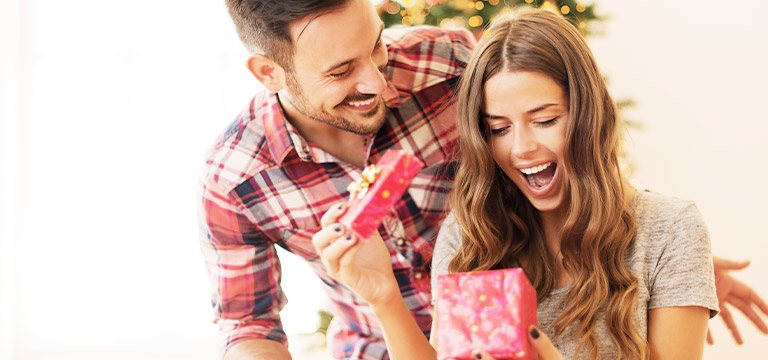 A woman beams excitedly as she opens a gift from her partner.