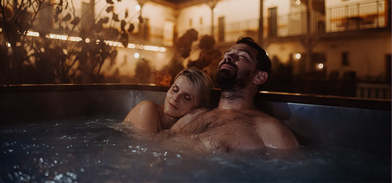 A couple snuggle happily together in an outdoor hot tub.